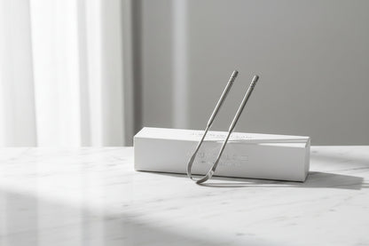 Auralis tongue scraper in stainless steel design surrounded by water droplets for daily oral care.